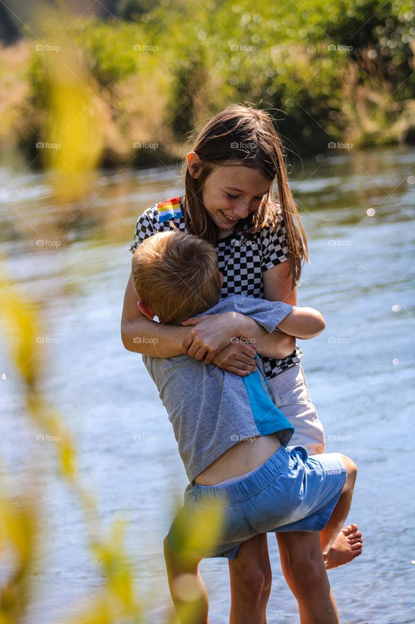 Brother and sister hugging alongside the river on a hot summer day 