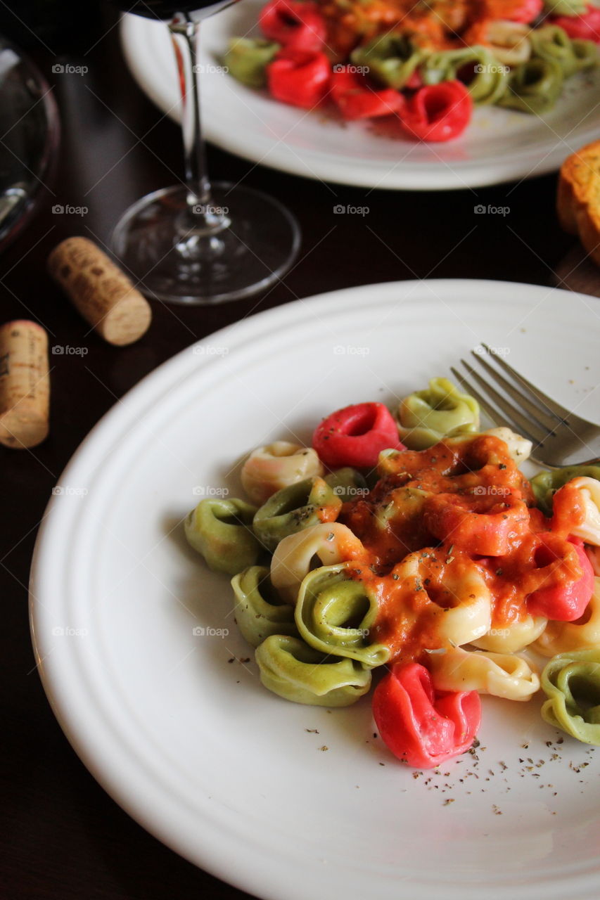 Italian inspired meal of tri-colored tortellini with red sauce and red wine.