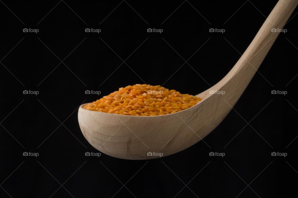 close up of lentil in a wooden spoon on black background