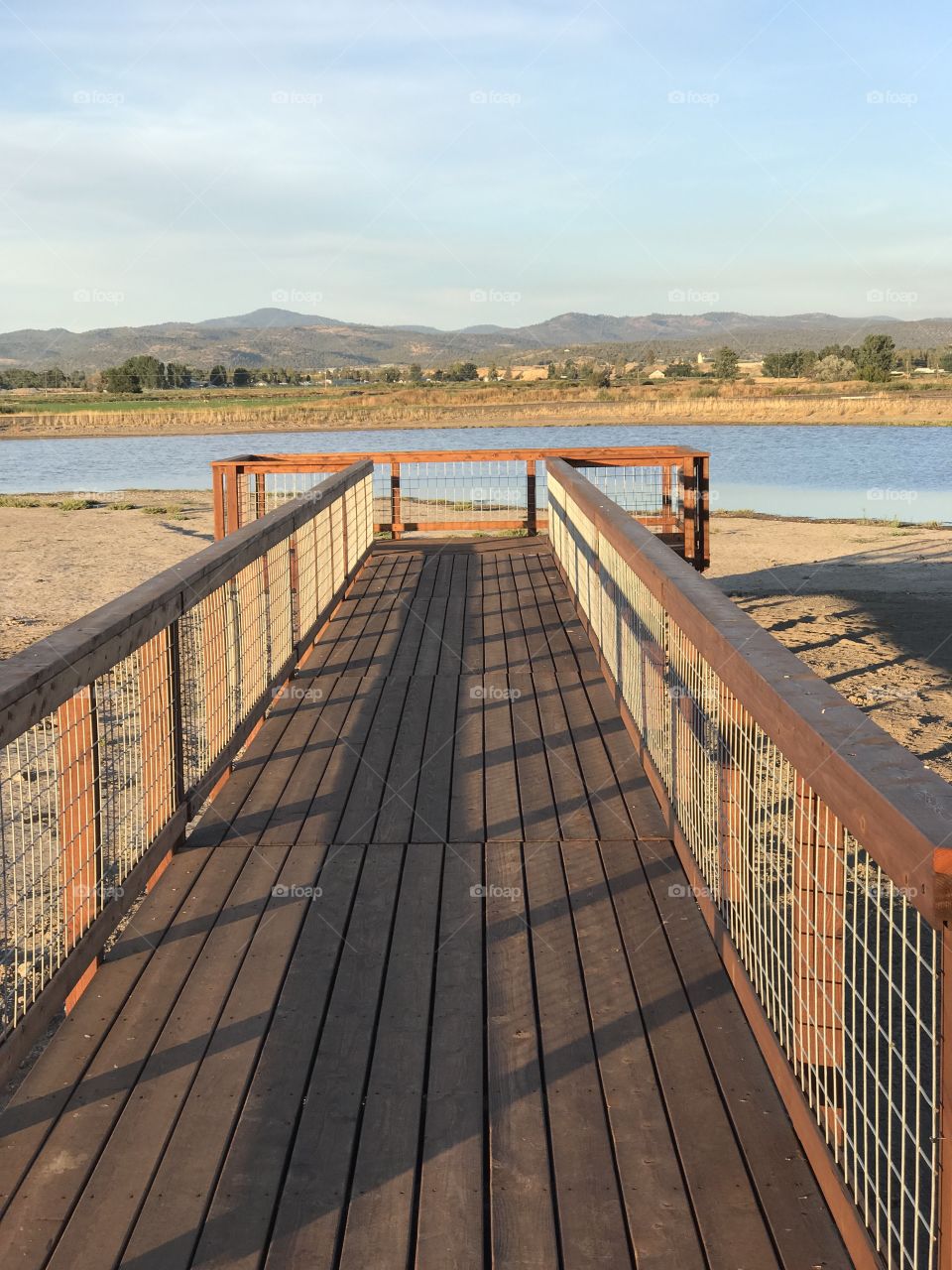 A wooden viewing bridge extends to a pond in a wildlife park outside of Prineville in Crook County in Central Oregon with the golden glow of evening on a fall day.