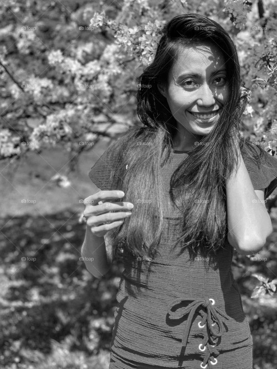 Portrait of young adult smiling woman standing in front of cherry blossoms in black and white. 