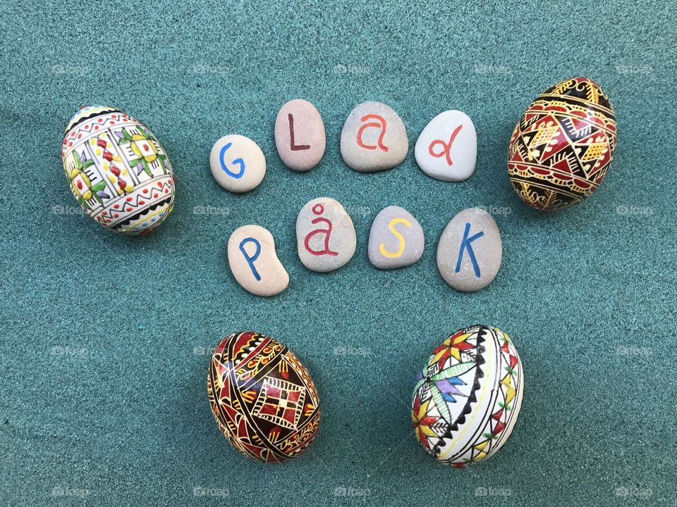 Glad Påsk, swedish Happy Easter with carved and colored stones and decorated eggs over green sand 