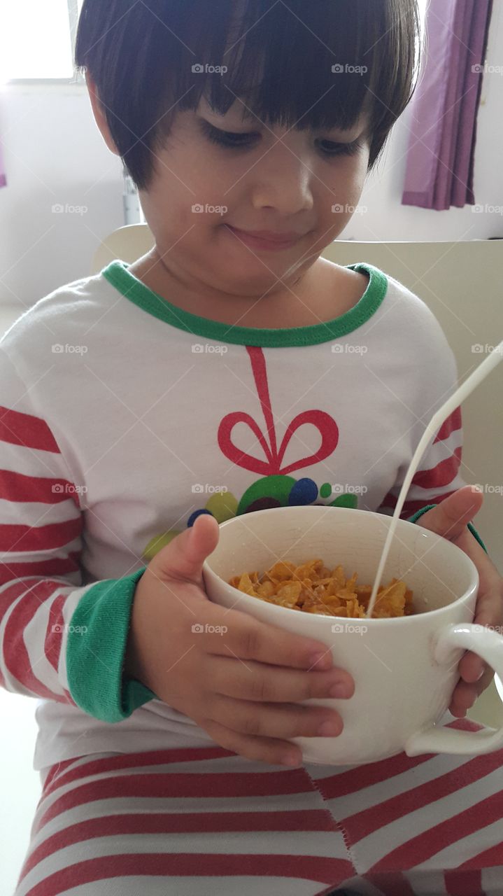 breakfast time. kid holding bowl of cereal while milk pouring over