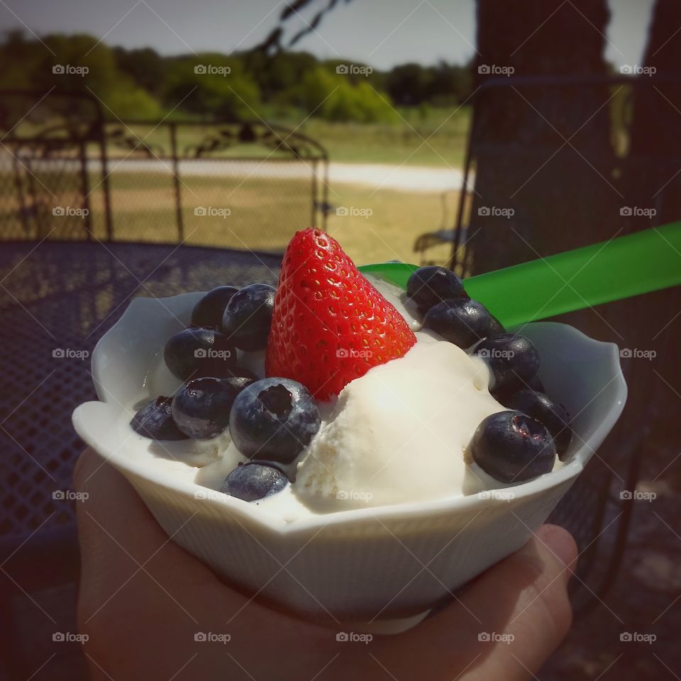 A strawberry and blueberries on top of homemade vanilla ice cream outside on a warm summers day