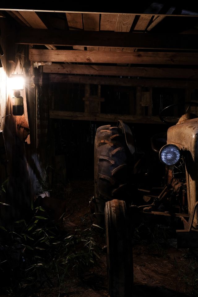 Partial front view of a 1953 Ford Jubilee vintage tractor that is still operational under the dim light of a lantern in an old barn. 