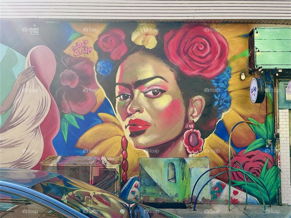 The Latina with a big red rose in her hair is part of an art mural that stretches over almost an entire city block at “Jefferson St” off “Broadway” in “Bushwick”, Bklyn near the “Myrtle Ave” “M” train station and overpass. 2024. Hypnotic Productions