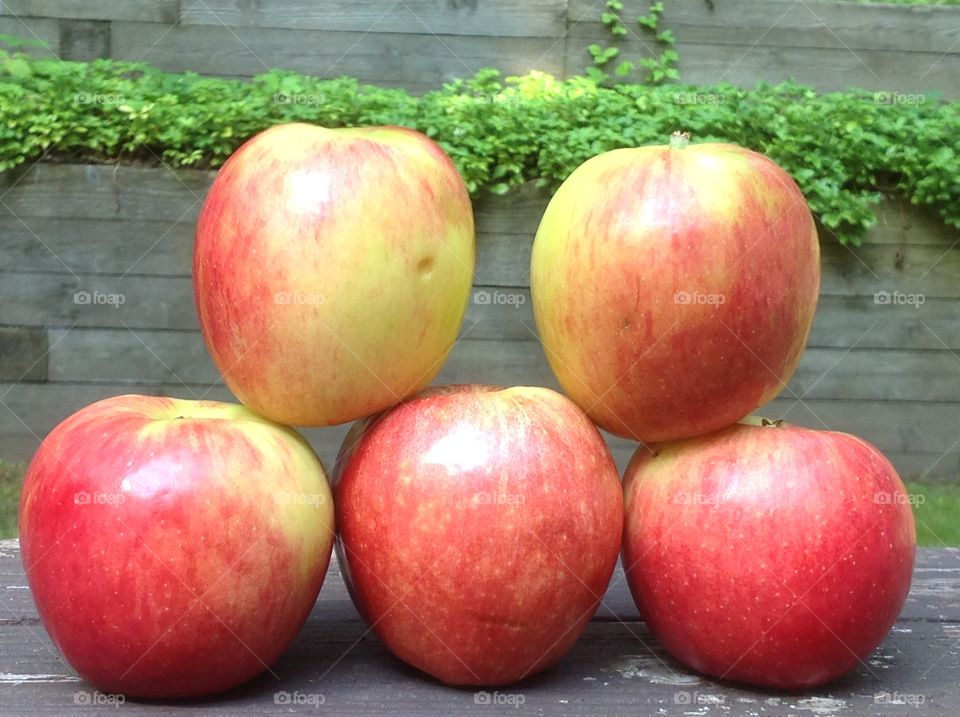 Apples stacked outdoors on wooden bench.