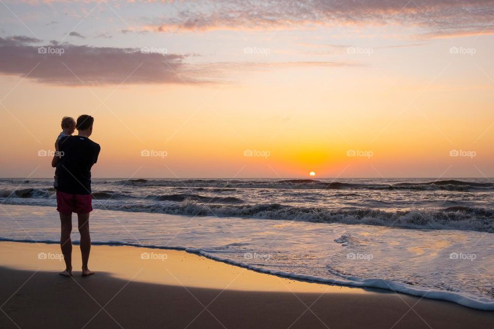 silhouettes of father and baby on sunrise ocean background,family concept