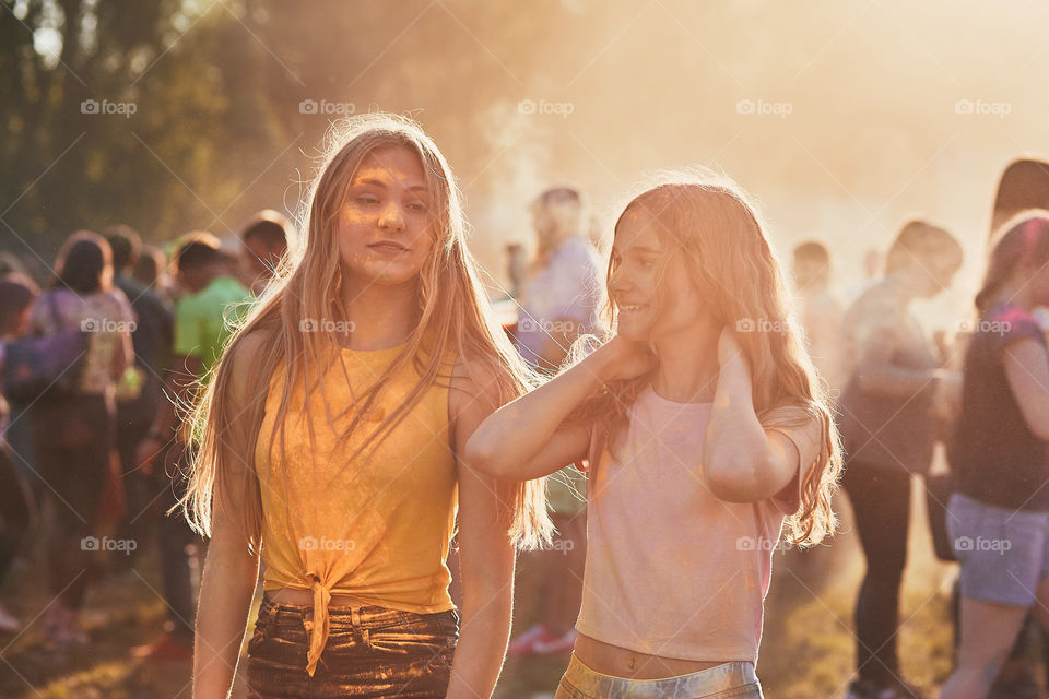 Portrait of happy smiling young girls with colorful paints on faces and clothes. Two friends spending time on holi color festival