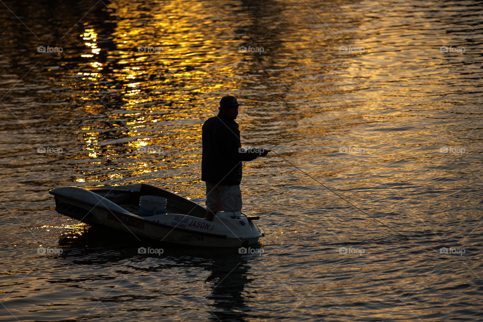 A man fishing on a lake at sunset
