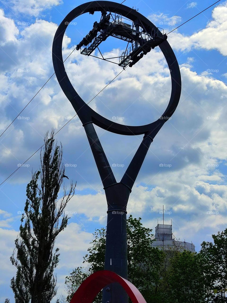 Ring of the cable car against a blue sky with white clouds and tops of green trees