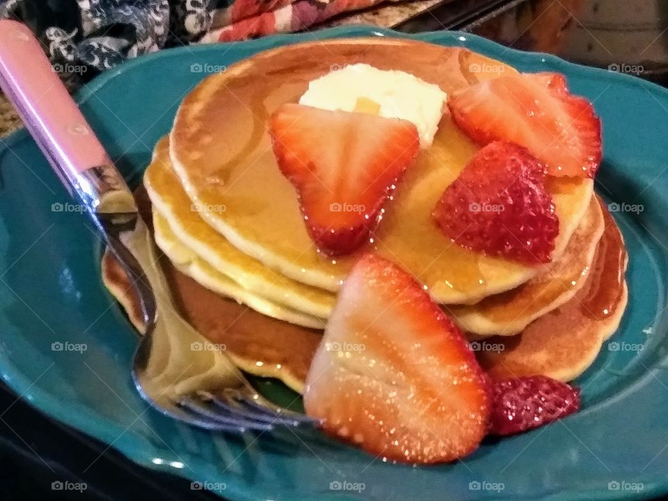 stack of pancakes with syrup, butter and strawberries