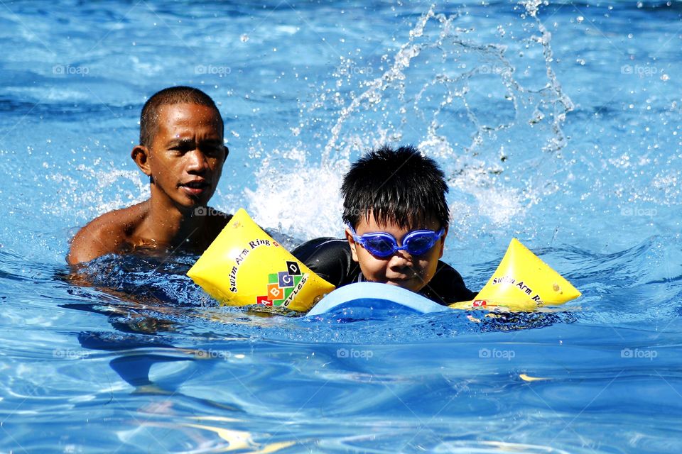 young kid learns how to swim with the help of a swimming coach