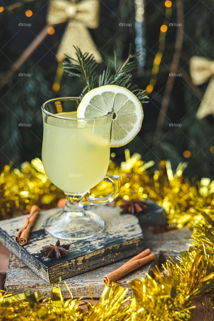 One glass of hot traditional ginger drink with cinnamon, anise and lemon slices on a cutting board, stands on a wooden table in golden tinsel on a blurred background, close-up side view. Traditional holiday drinks concept.