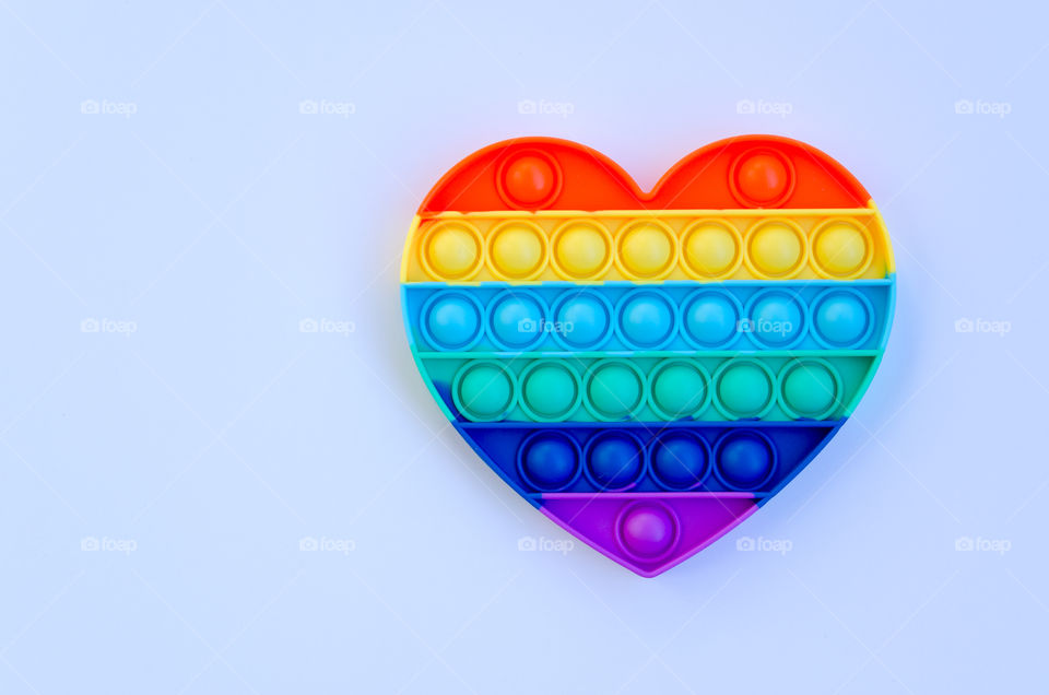 Top view of anti stress sensory toy Pop it rainbow heart on white background. Popular, trend toys in 2021