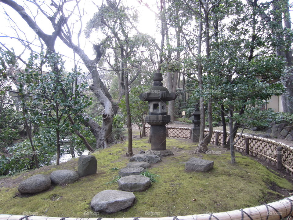 Asakusa Kannon. Sensoji Buddhist Temple and Gardens. Tokyo, Japan. Stone Lantern and Stepping Stones Among Trees, Surrounded by a Small Fence