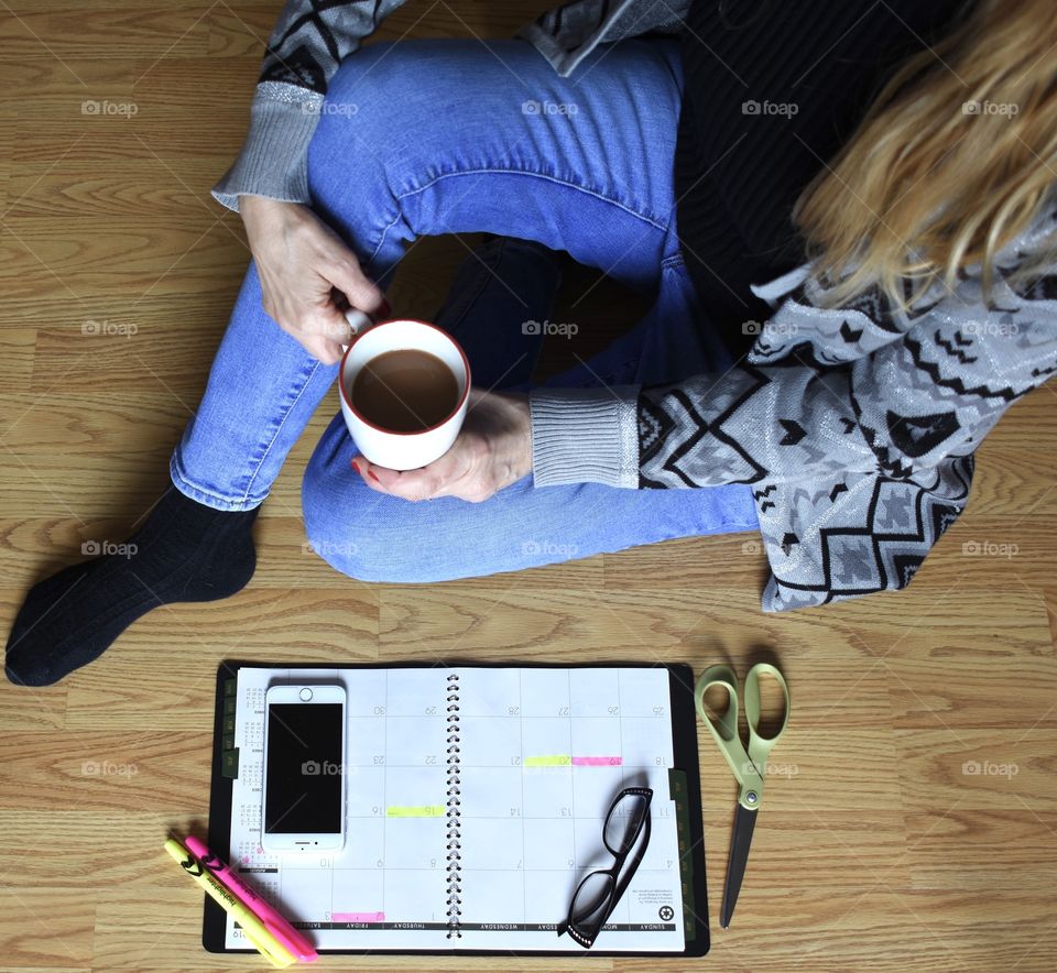 Cell phone electronics on calendar with woman with a cup of coffee sitting on floor 