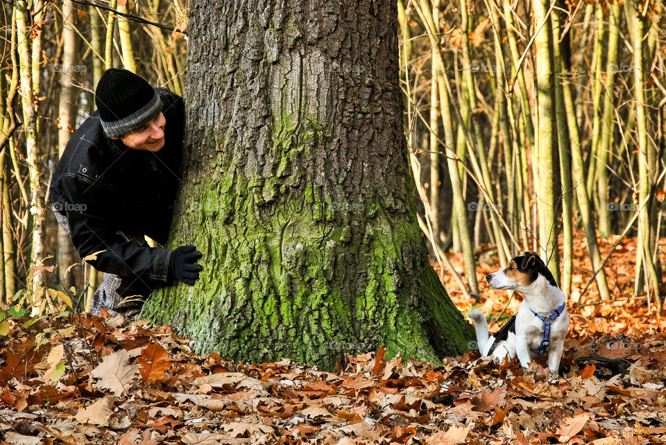 Man playing with his puppy near tree trunk