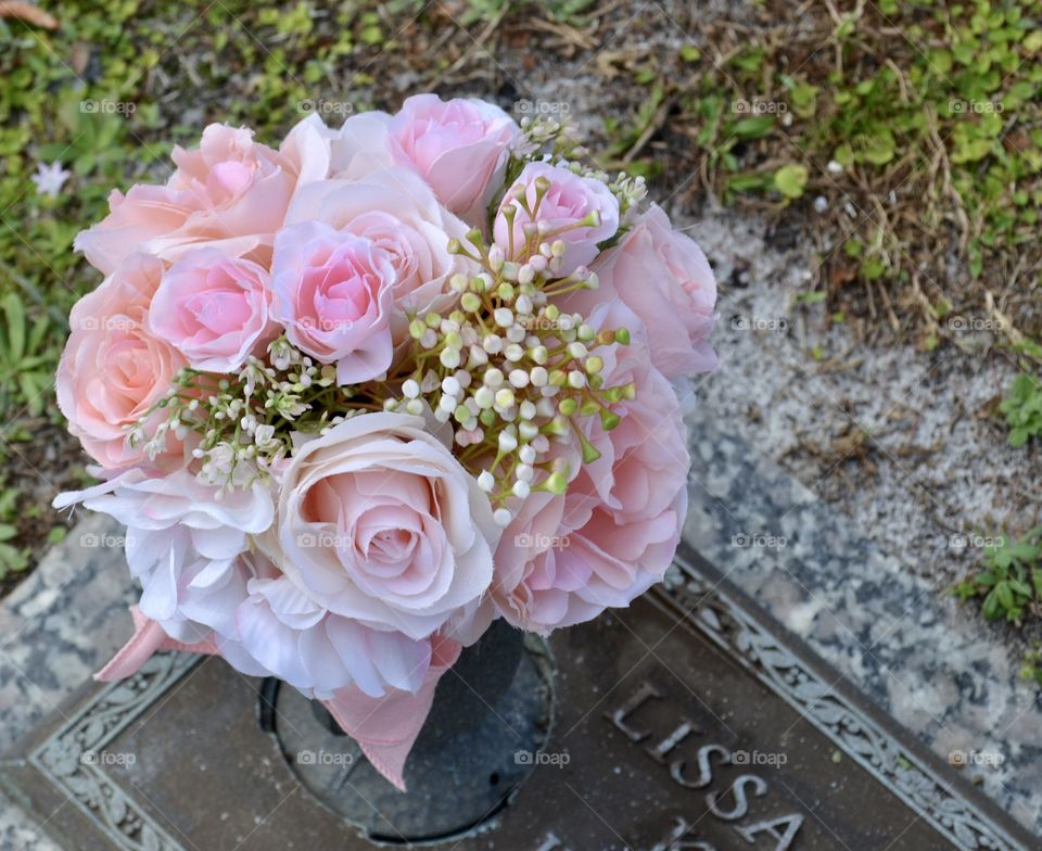 An off-centered view of a bouquet of pink roses on a gravestone 