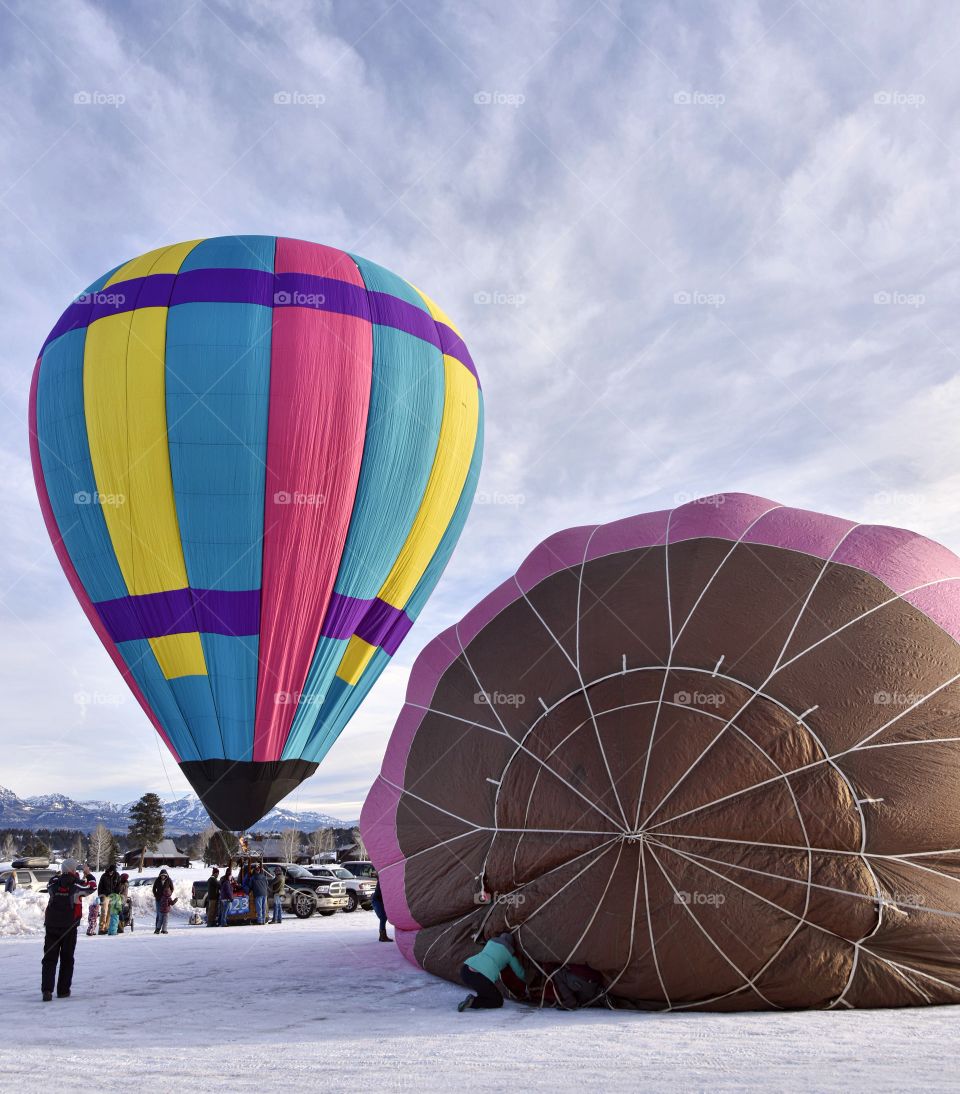 A hot air balloon festival in the winter creates a colorful scene. Everyone is setting up for launch.