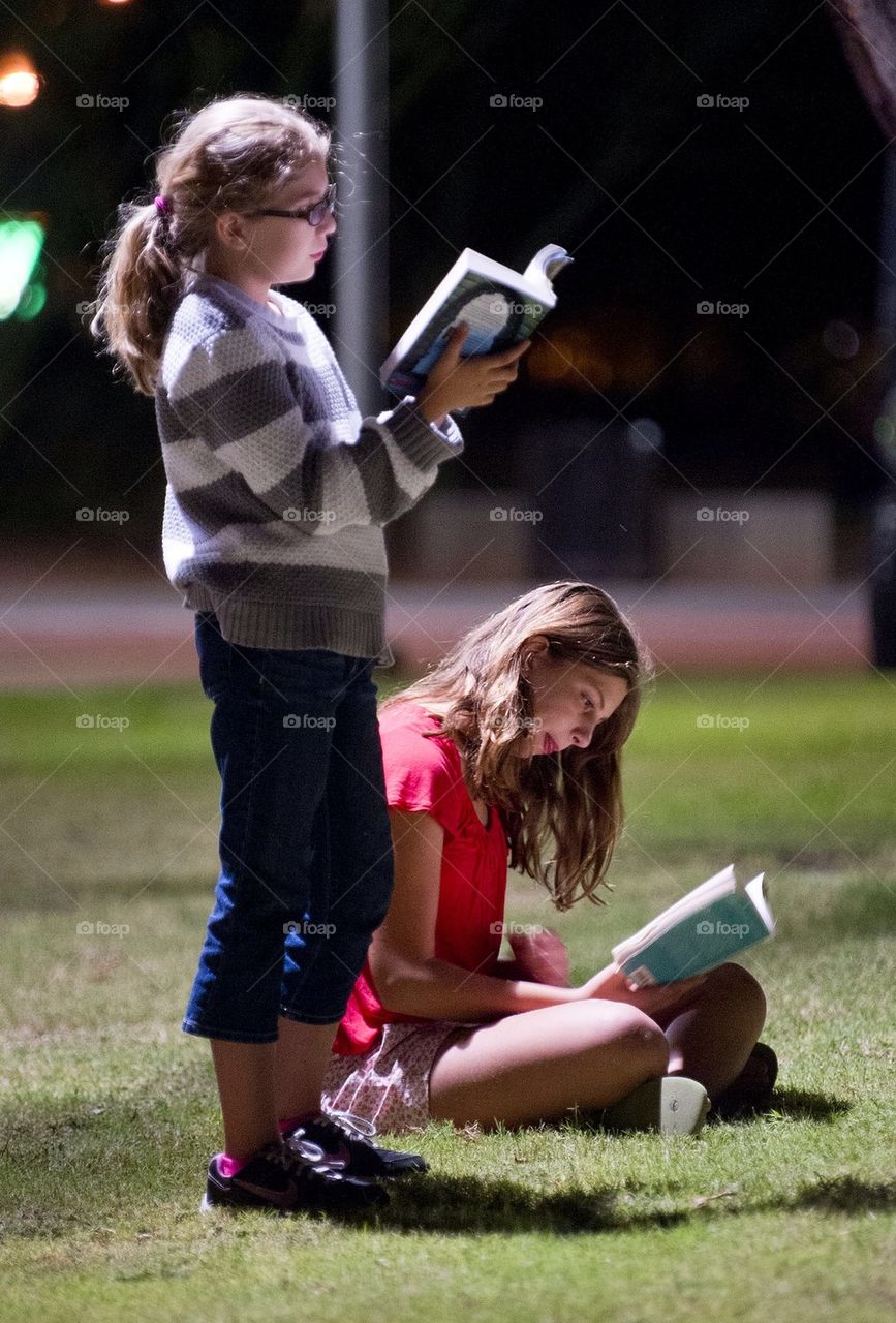 Two girls chose a book over a smart phone. As they read at night in a