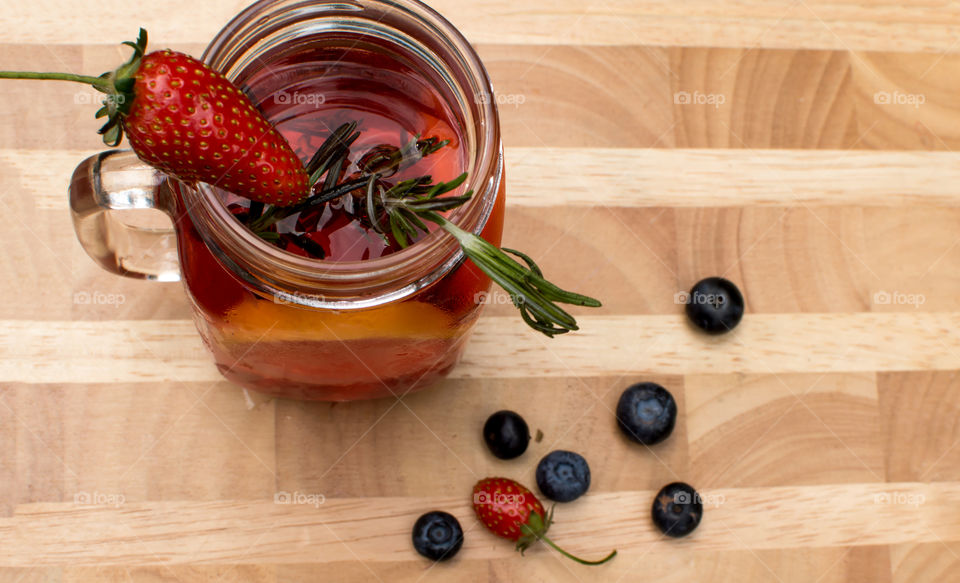 Flavored water with rosemary, citrus and fresh garden berries garnish with strawberry for aromatic and healthy summertime home made juice on wood background elevated view 