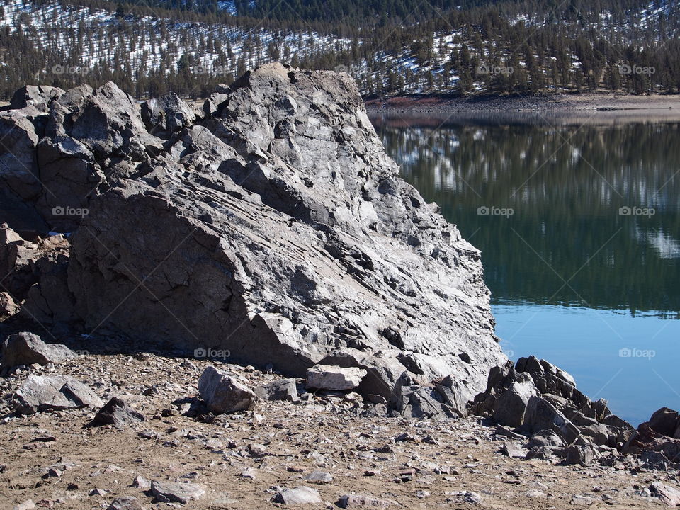 Jagged rocks and boulders along the shoreline of Ochoco Lake in Central Oregon on a sunny spring day.