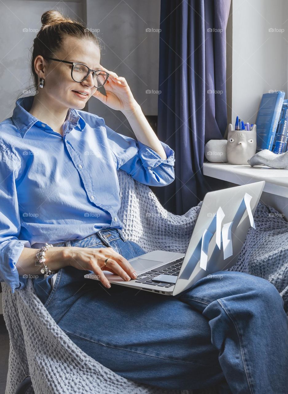 Woman in blue outfit working on laptop from home 