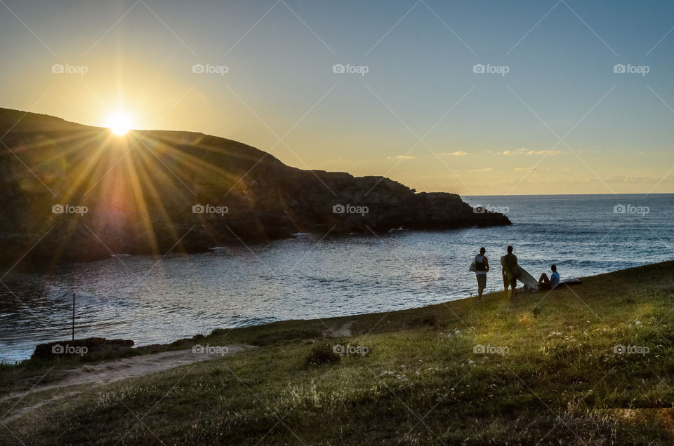 Sufers looking at the ocean as sun goes down 