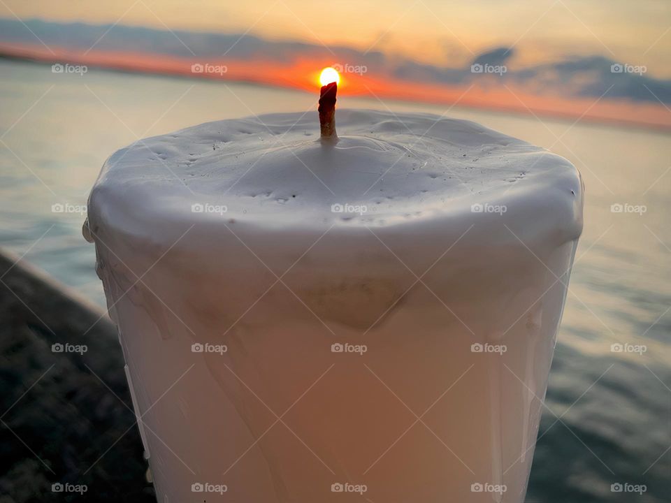 Candle Seems To Be Lit Up With A Small Flame From The Sun Setting By The Water In The Horizon.