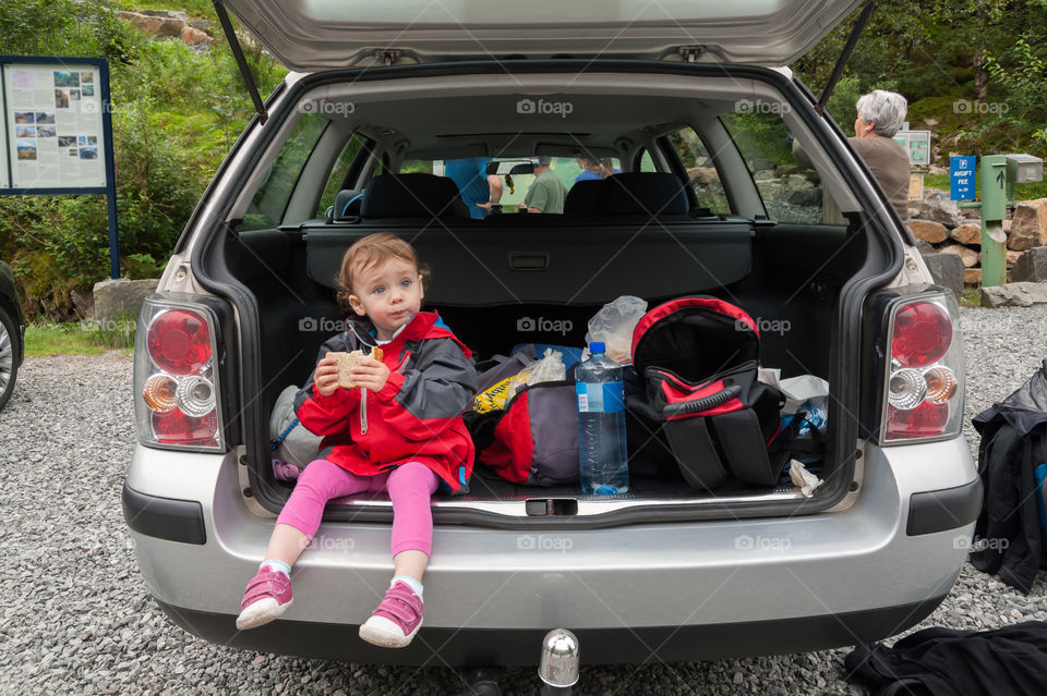 Small traveller sitting in a car boot and having a well deserved break for snack after trip into nature.