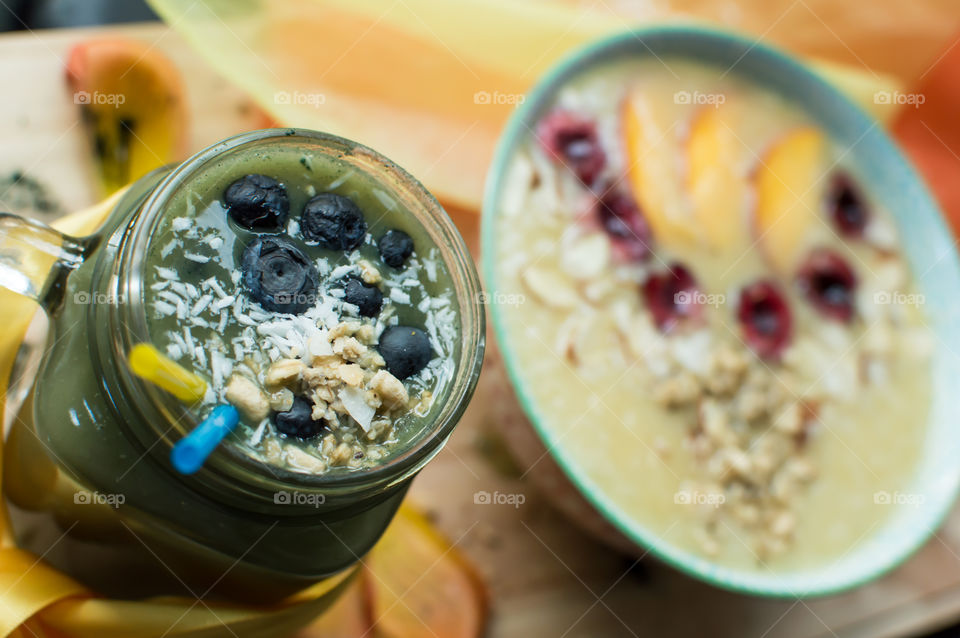 High angle view of green smoothie with blueberry, oatmeal  and coconut in glass with straws on table with smoothie bowl healthy eating artisanal food photography background 