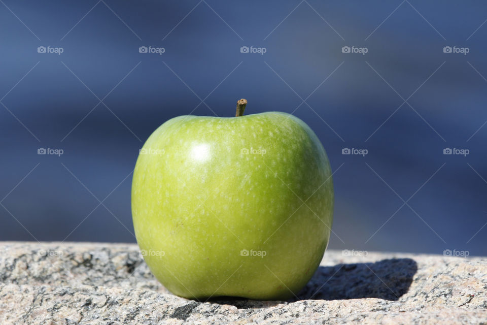 Green apple on the rocks against sky