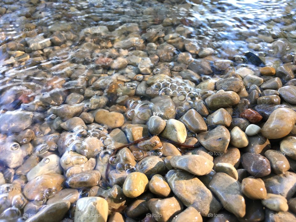 Small waves with bubbling water washing over stones turning them into smooth pebbles symbolic power of nature and water tranquility zen background 