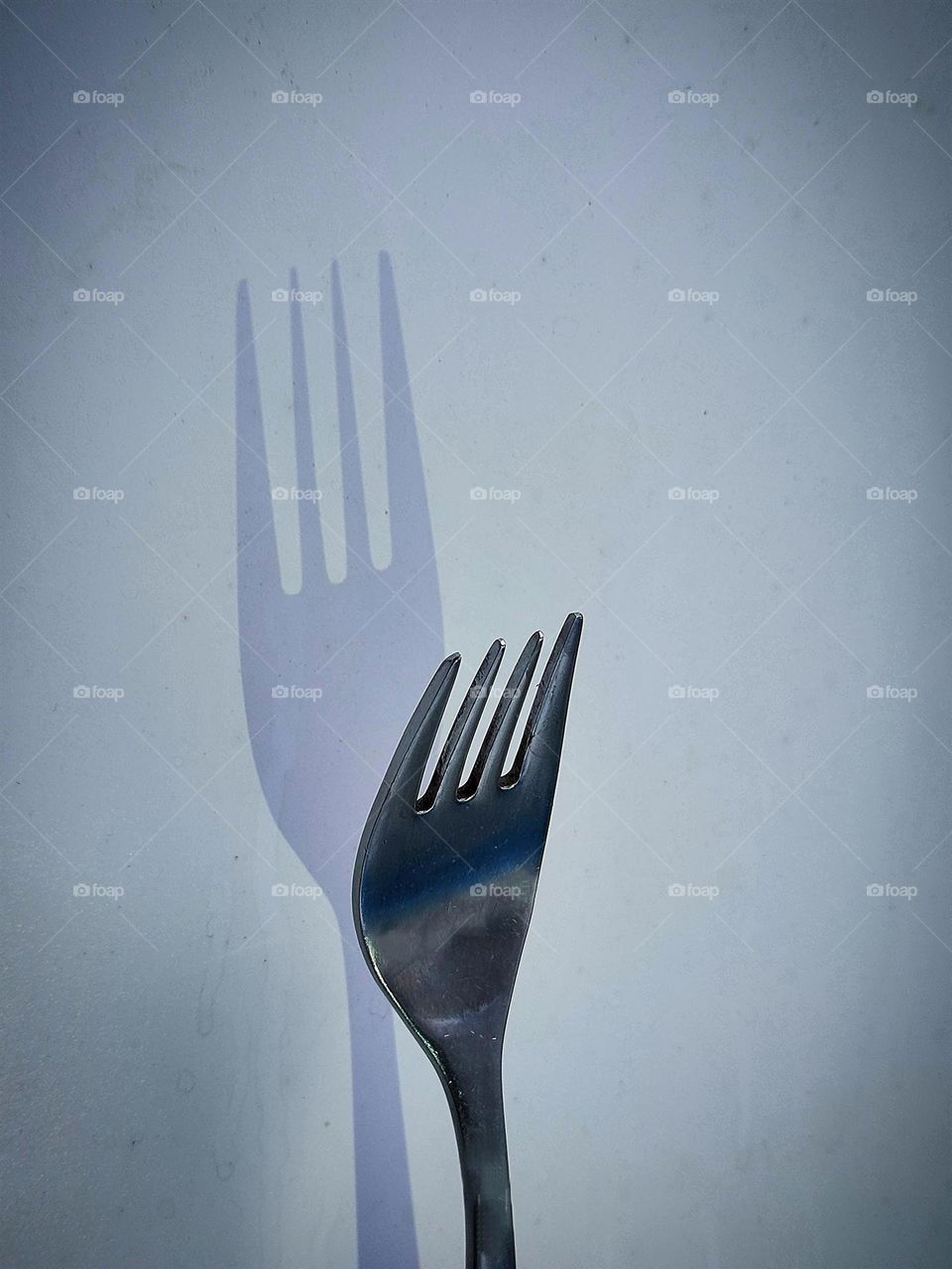 Creative forks.  On a white background a metal fork.  The direction of the light changes the shape of the shadow of the fork