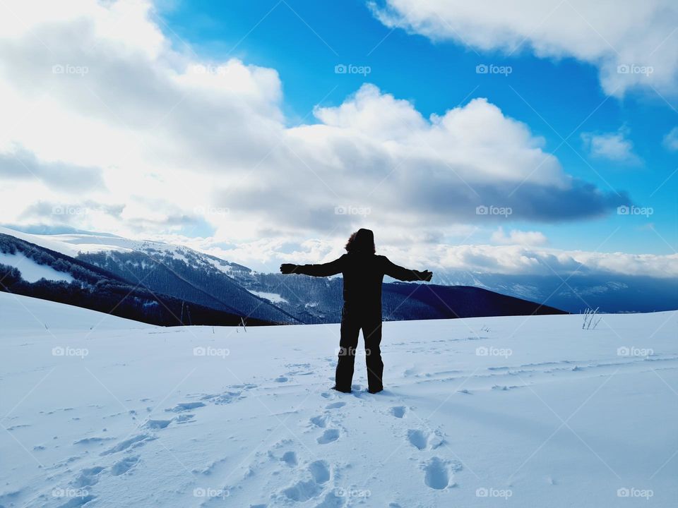 man from behind with open arms is lost in the magnificent snowy and winter landscape