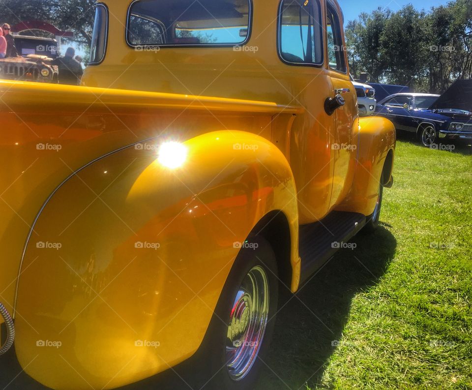 Rear view of a bright yellow restored vintage pickup truck at an outdoor car show