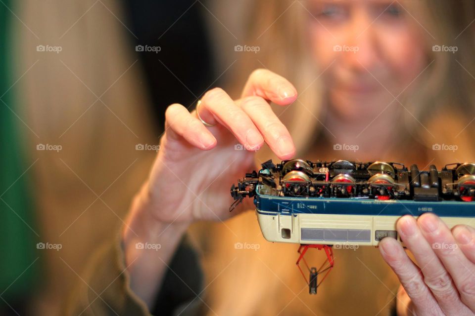 A woman checks the wheels and axles of a model train with her fingers