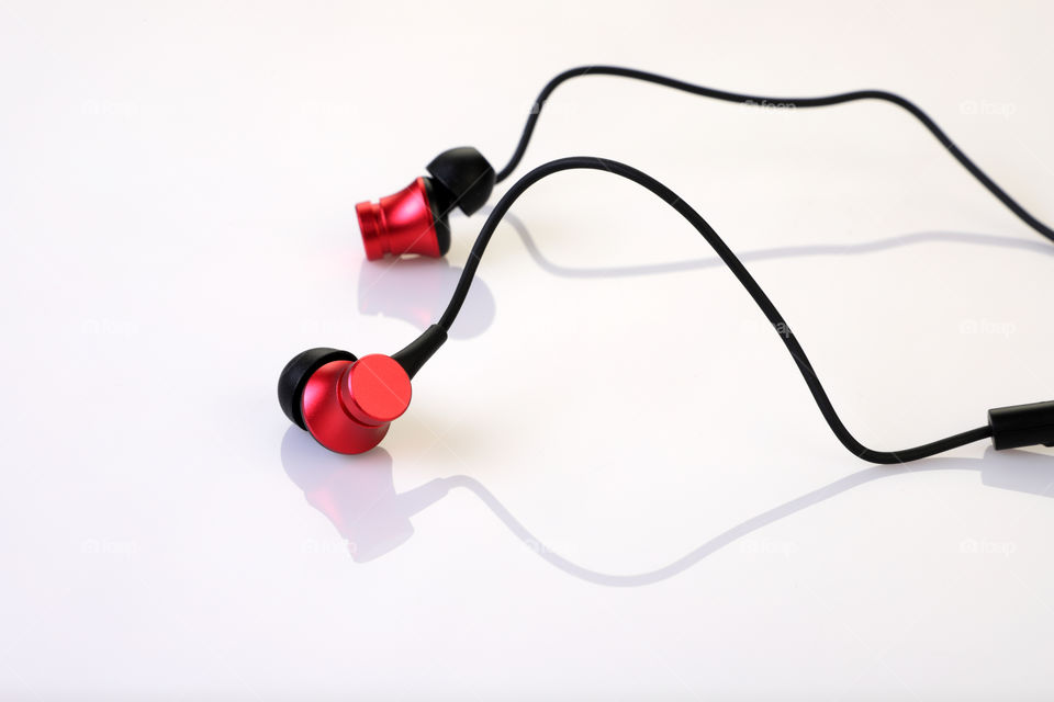 Red colored in ear  wired music earphones on white reflective background