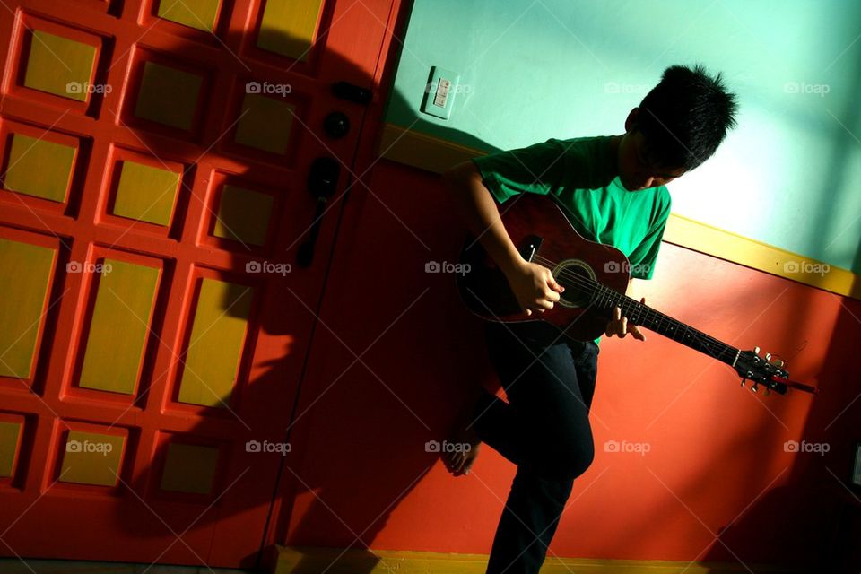 young asian teen playing guitar in a living room