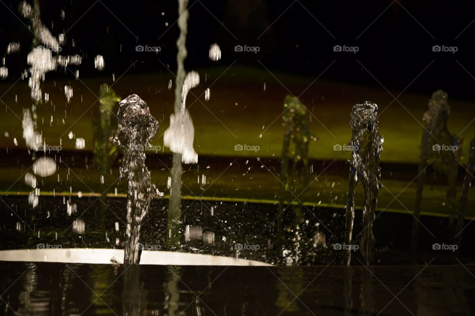 Silhouettes of water in motion in fountain with light reflections like people walking away abstract water art photography background 