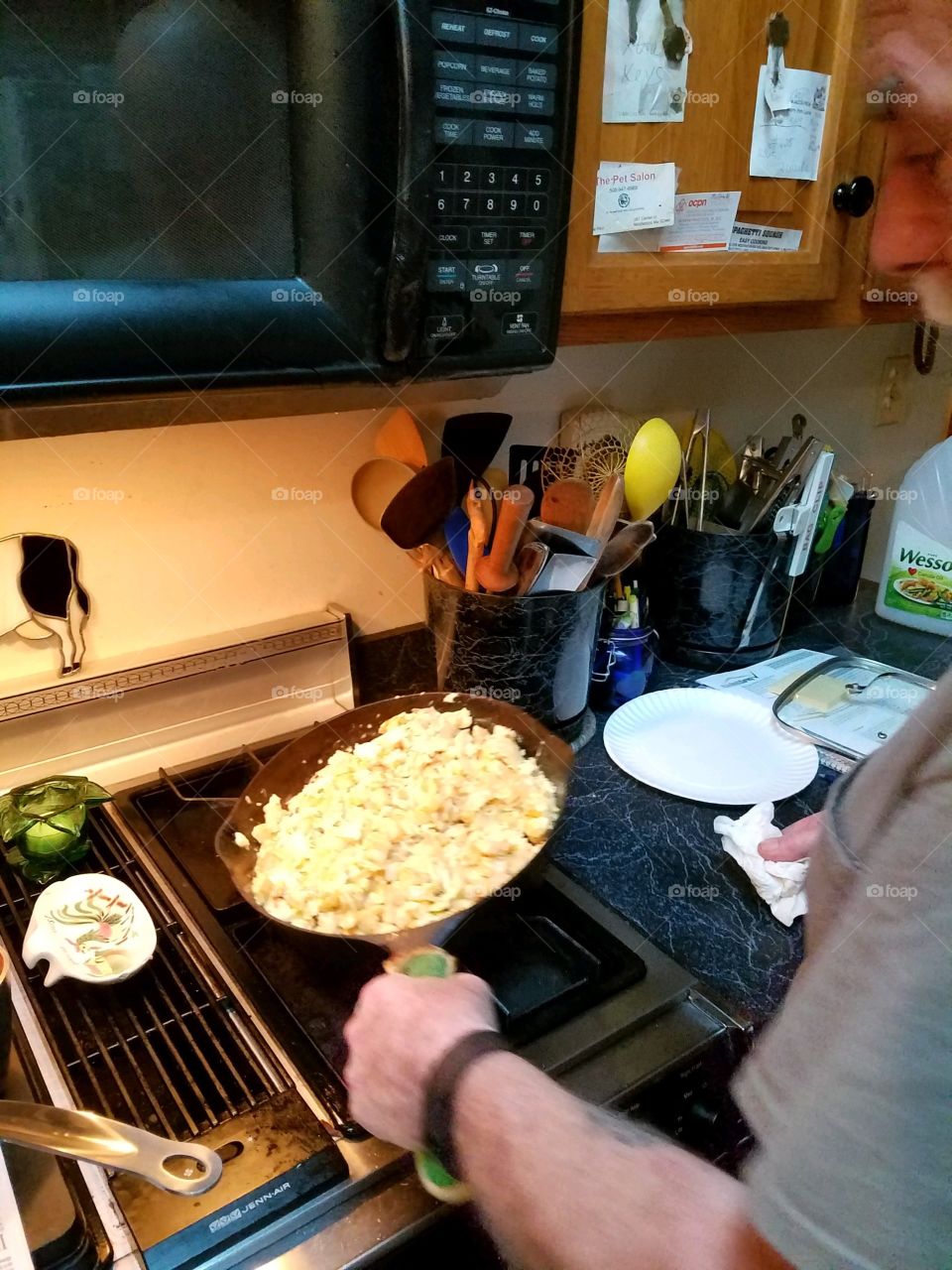 Man cooking scrambled eggs in frying pan on the stove. He's cooking breakfast.