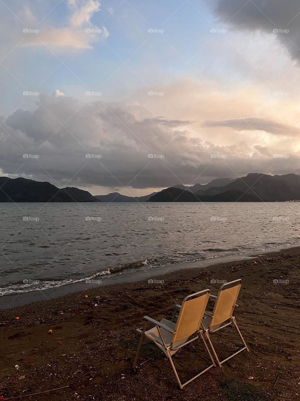 Sunset on rainy day, two chairs on the sand beach