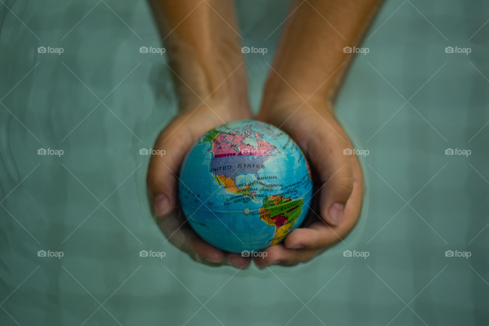 overhead looking down on hands holding world sphere showing North and South America continents