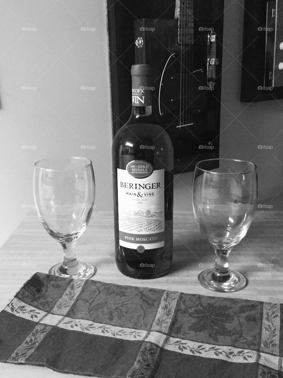 Black and white photo of a bottle of red wine, two glasses  and a clothe on a table