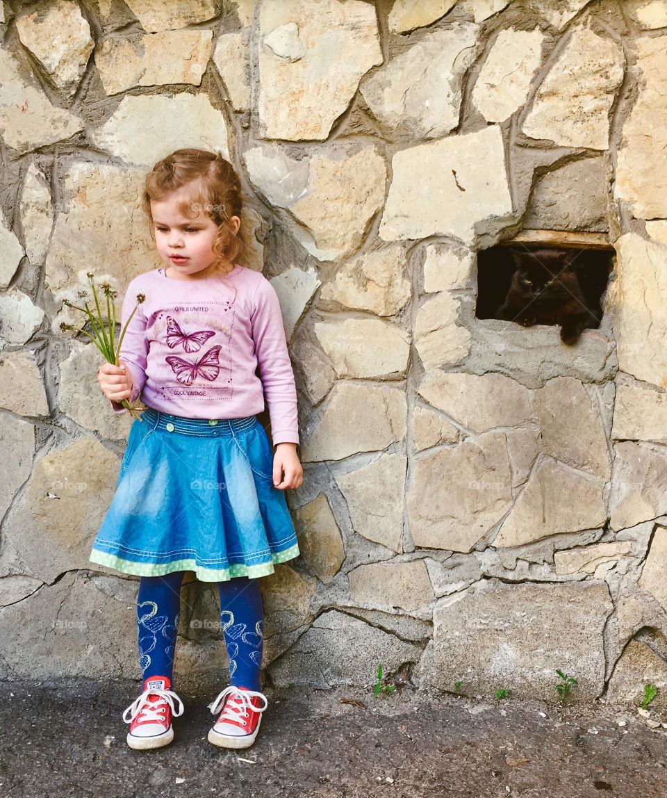 Cute curly girl standing by the wall with black cat. 