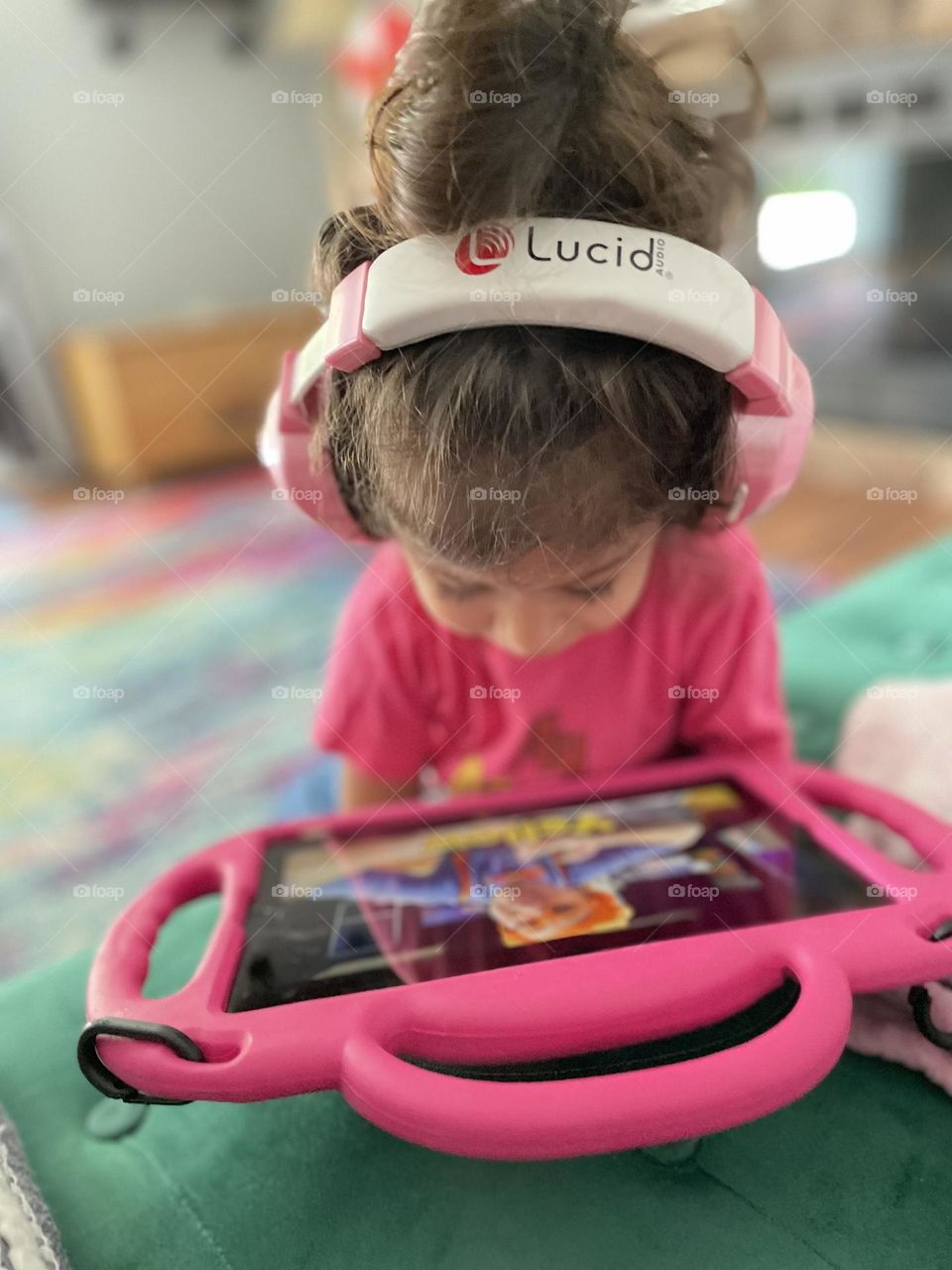 Toddler girl watches pink iPad with pink headphones and pink shirt, celebrating the Barbie style, toddler watches iPad, toddler entertained by technology 