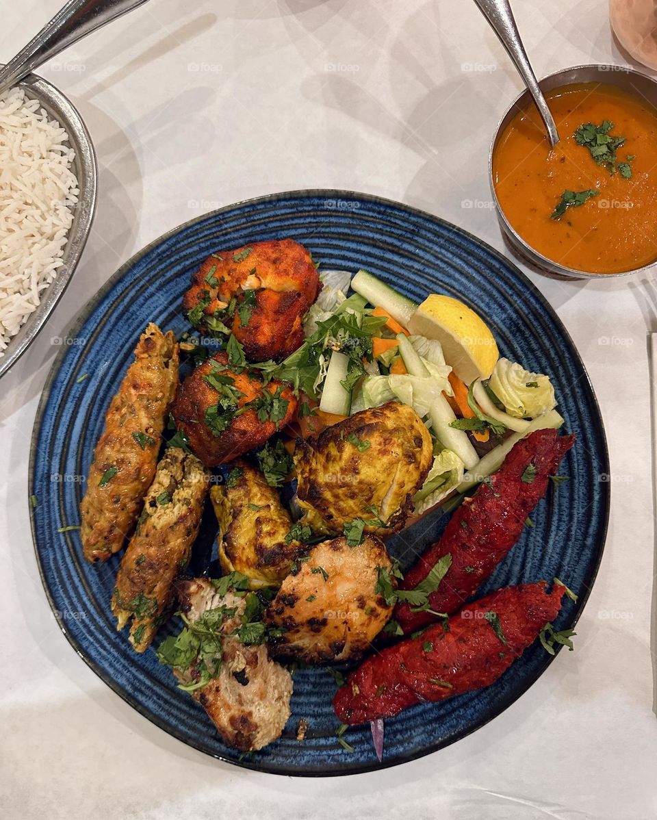Delicious mixed grill that consist of tandoori chicken, grilled salmon, grilled lamb, Chicken tikka and the like. An Indian cuisine on a blue round plate.