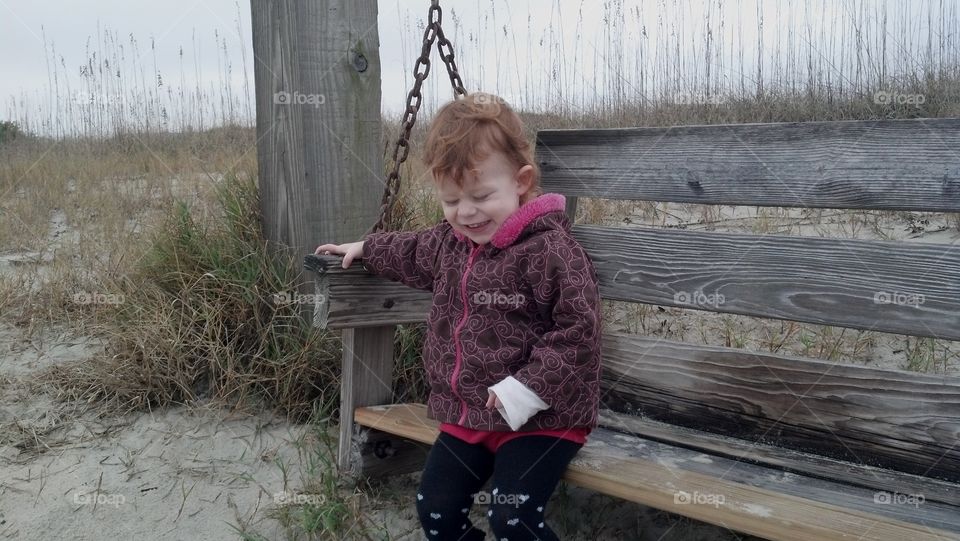 at the beach. my daughter sitting on a swing at the beach