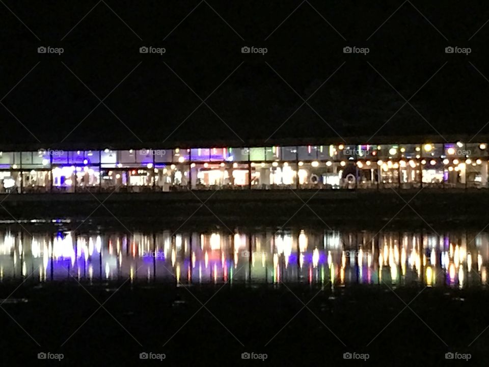blurred photography of shopping buildings when turn on the lights in night time with its colorful shadow reflects on lake surface, using as background